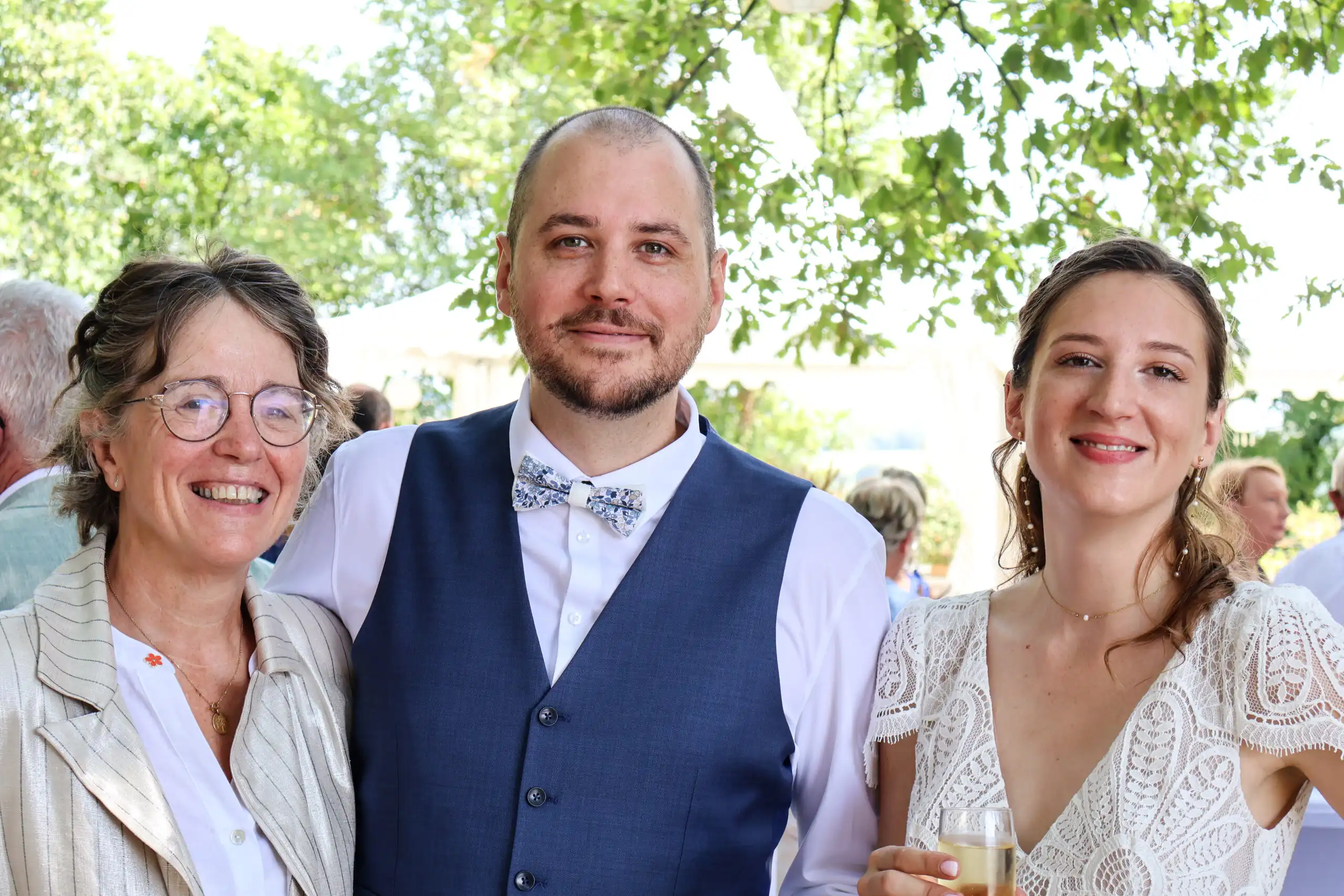 deux invités et une mariée souriants posant ensemble en extérieur